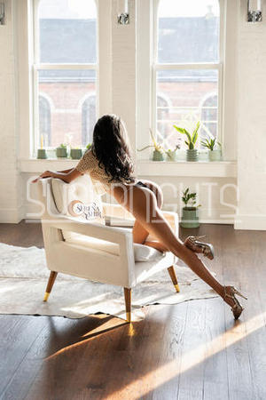 Serena Sahir posing on a chair beside a sunlit apartment window.